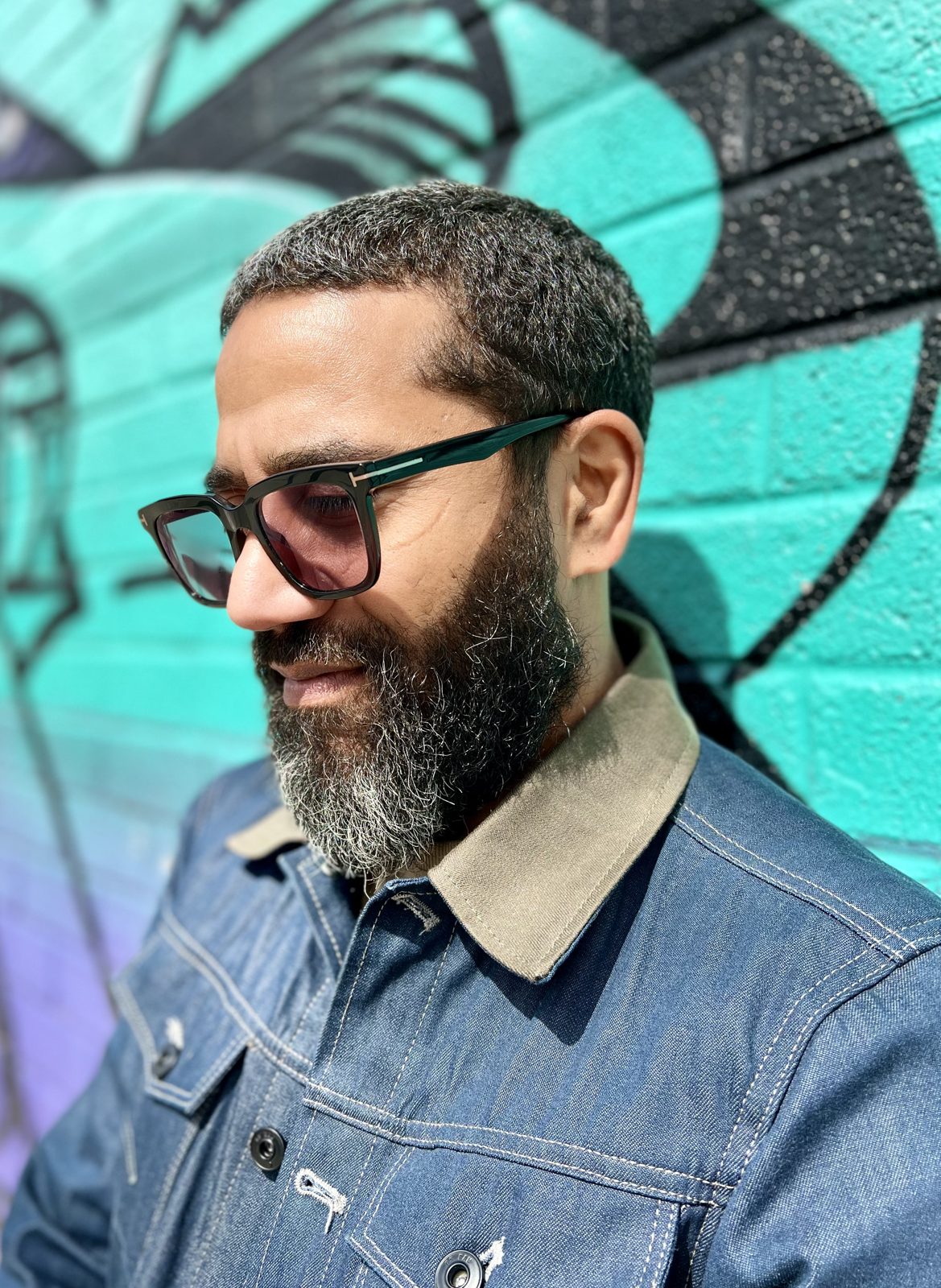 Danny Deleon in a denim jacket against a teal graffiti wall